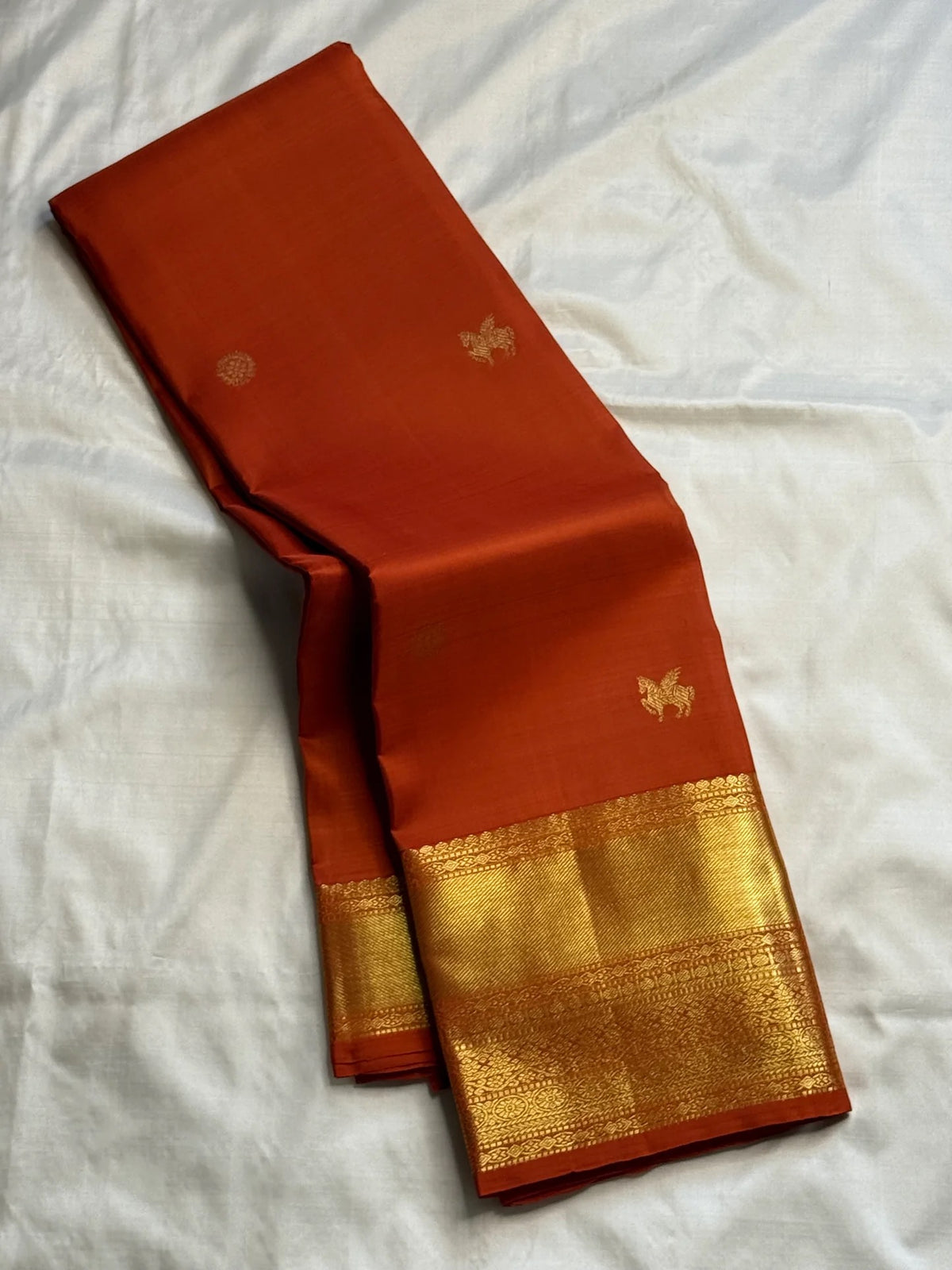 Full view of the earthy burnt-orange Pure Silk Kanjivaram Butta saree with broad gold zari border