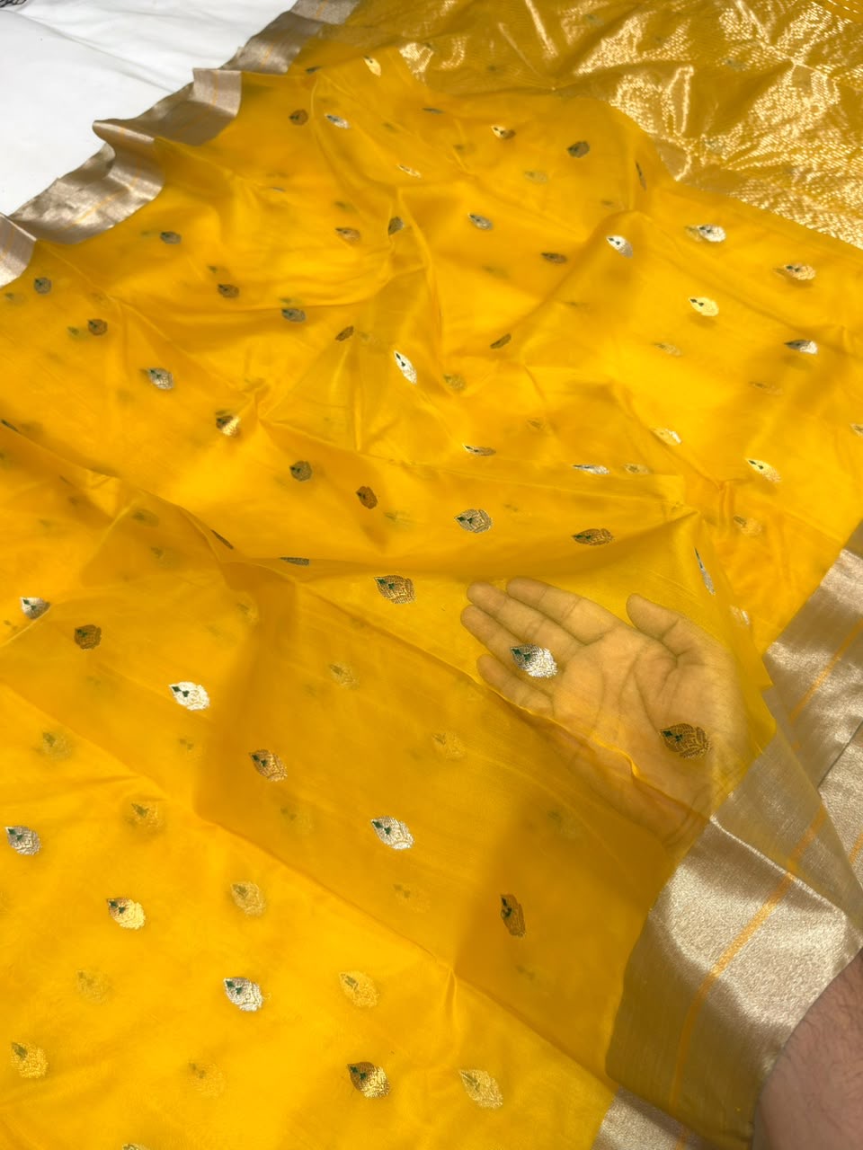 Close view of the turmeric yellow Chanderi body with pale buttas and green accents near the silver-toned border