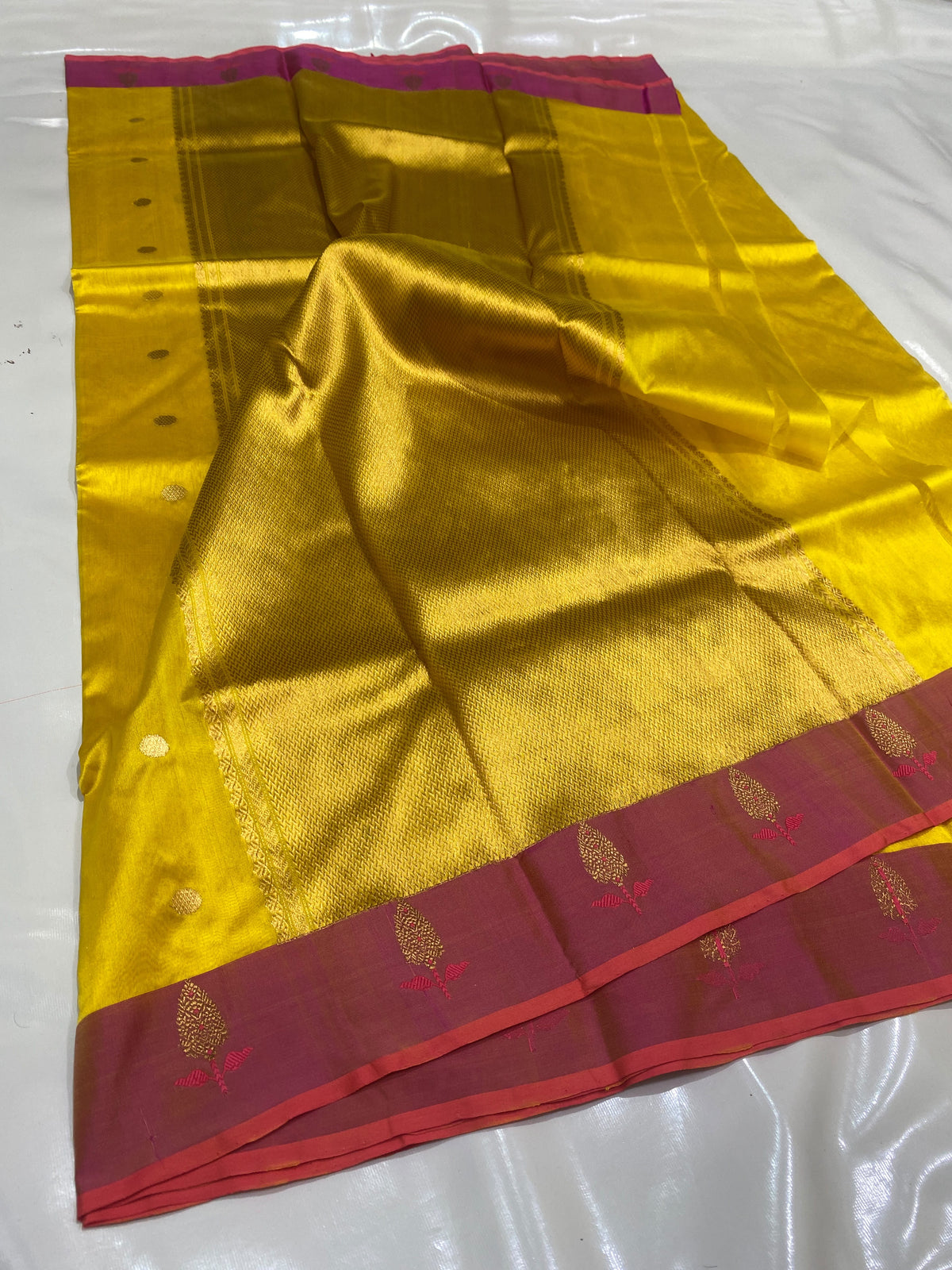 Turmeric yellow Chanderi saree laid open showing the raspberry pink border and rich golden pallu