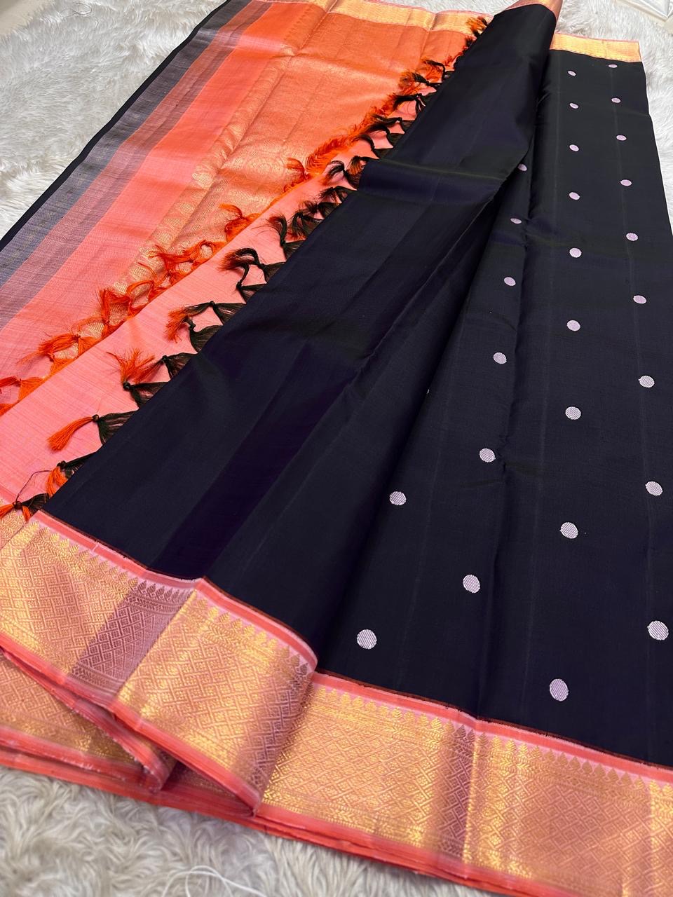Folded pure Kanchipuram silk saree in purple black tones showing silk texture and shimmering zari border detail.