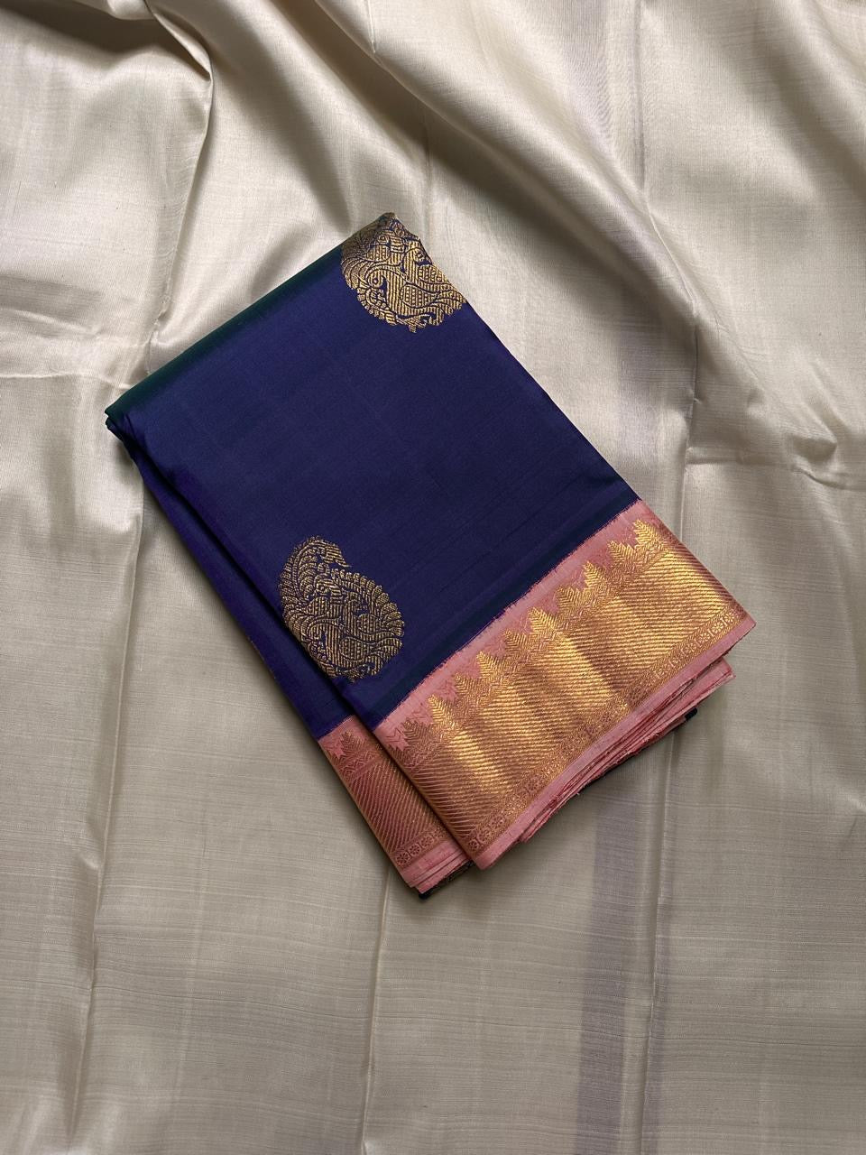 Folded navy Kanchipuram silk saree with gold zari buttas and blush pink zari border