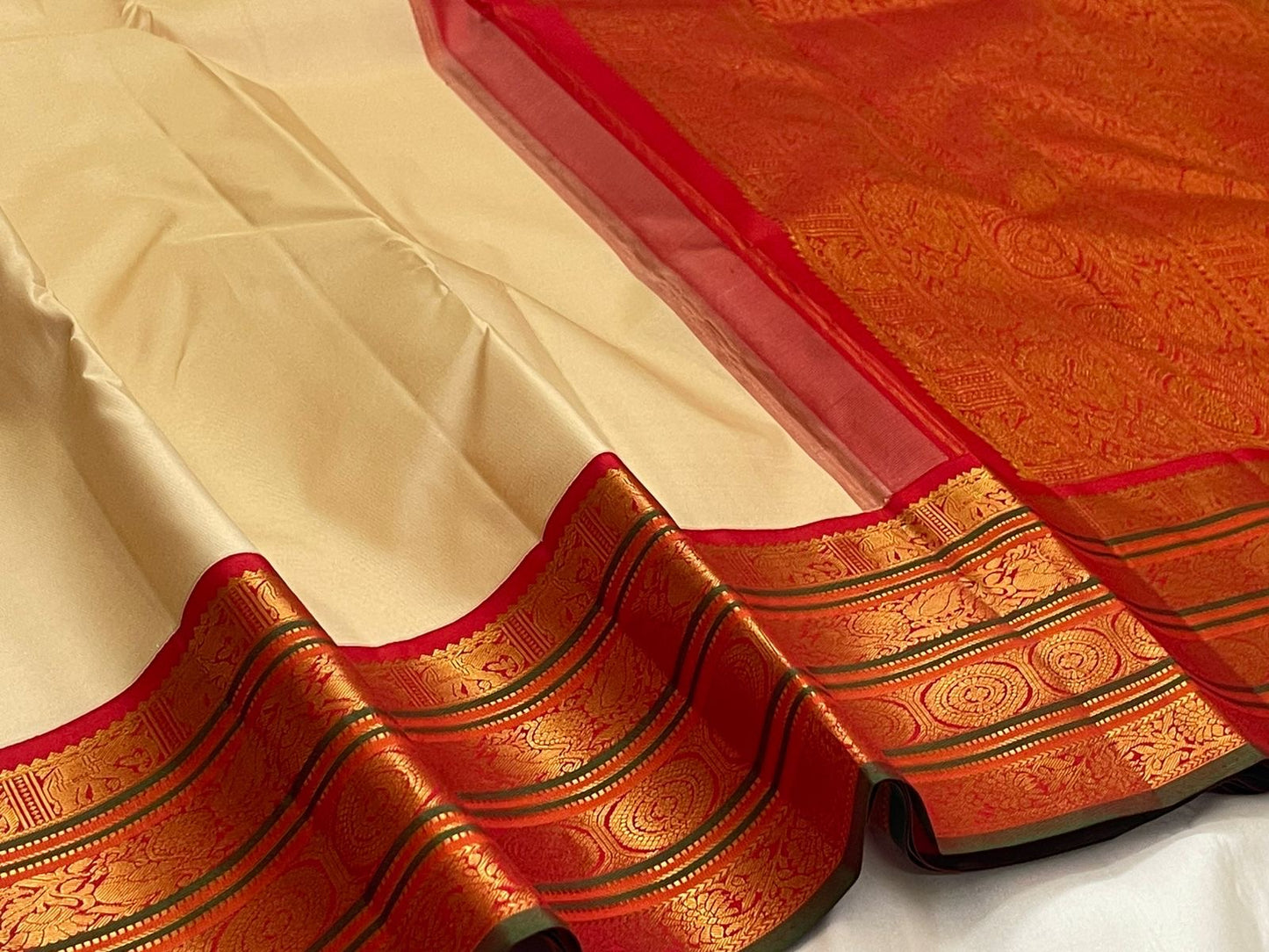 Close-up of red zari woven border with green edging on an ivory pure Kanchipuram silk saree, with tassels visible.