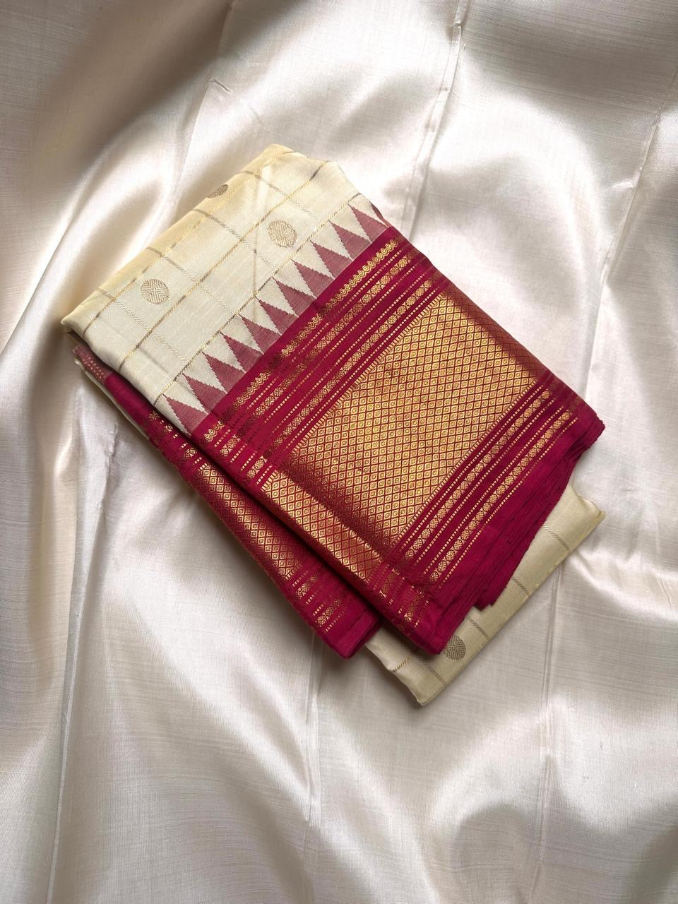 Folded ivory Pure Kanchipuram silk saree with kattam checks, zari buttas, and a tomato red zari woven border.