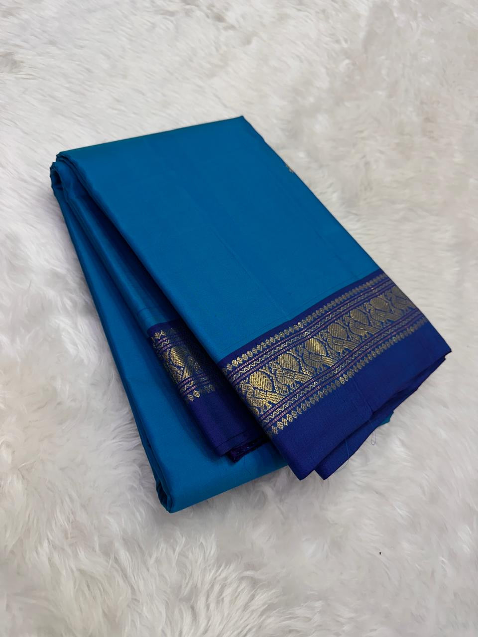 Folded ink blue Pure Kanchipuram Silk Saree with navy zari border on white fur background