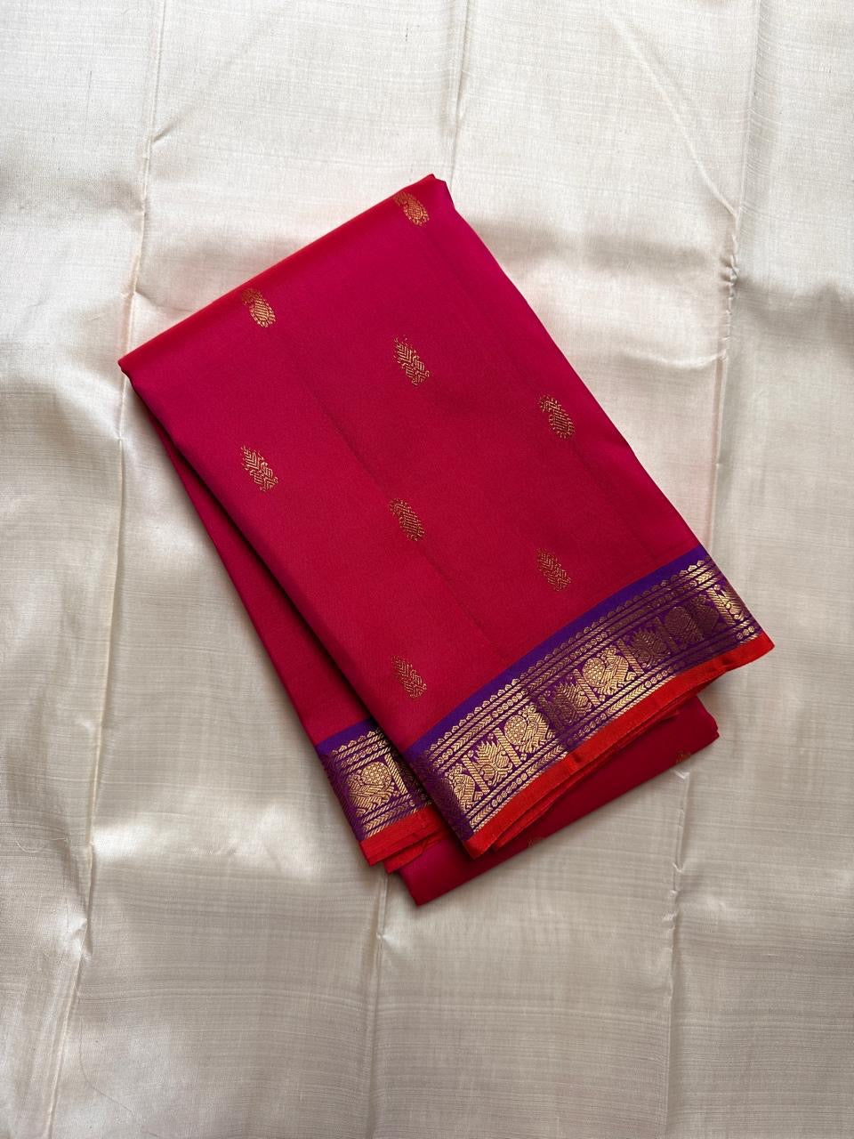 Pure Kanchipuram silk saree folded in rani pink with small gold zari buttas and a blue zari woven border.