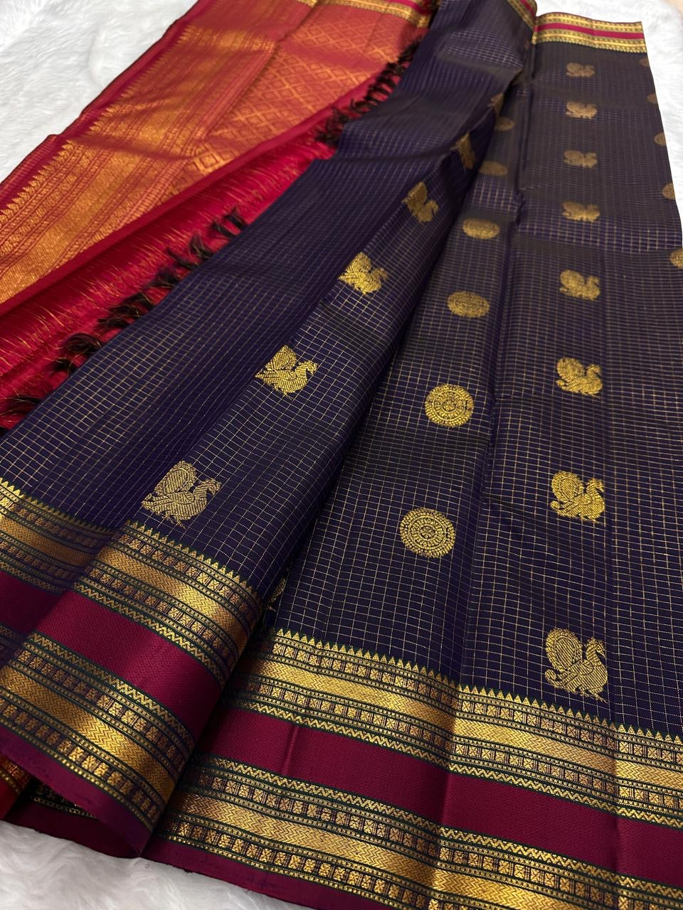 Deep plum purple Pure Kanchipuram silk saree folded lengthwise showing gold zari woven motifs and maroon zari woven border on white backdrop