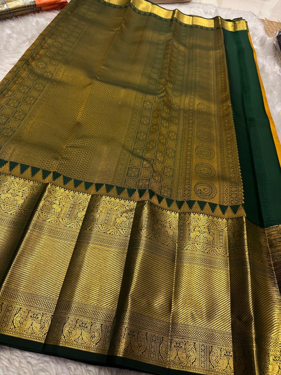 Close-up of gold zari woven border with deep green edging beside the red saree body on a light fabric background.