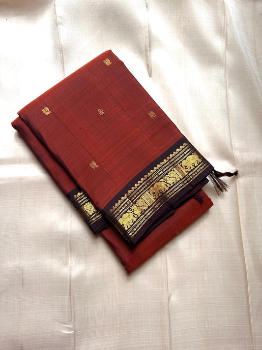 Pure Kanchipuram silk saree folded in rust tone with black zari woven border, shot on ivory fabric backdrop, shipped from New Jersey USA.