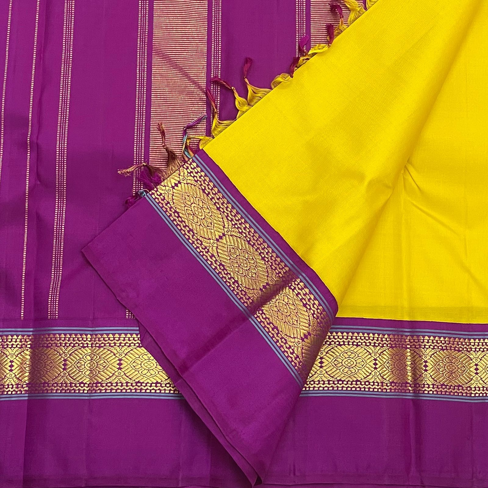 Folded yellow and purple pure Kanchipuram silk saree on purple pallu with zari stripes and tassels
