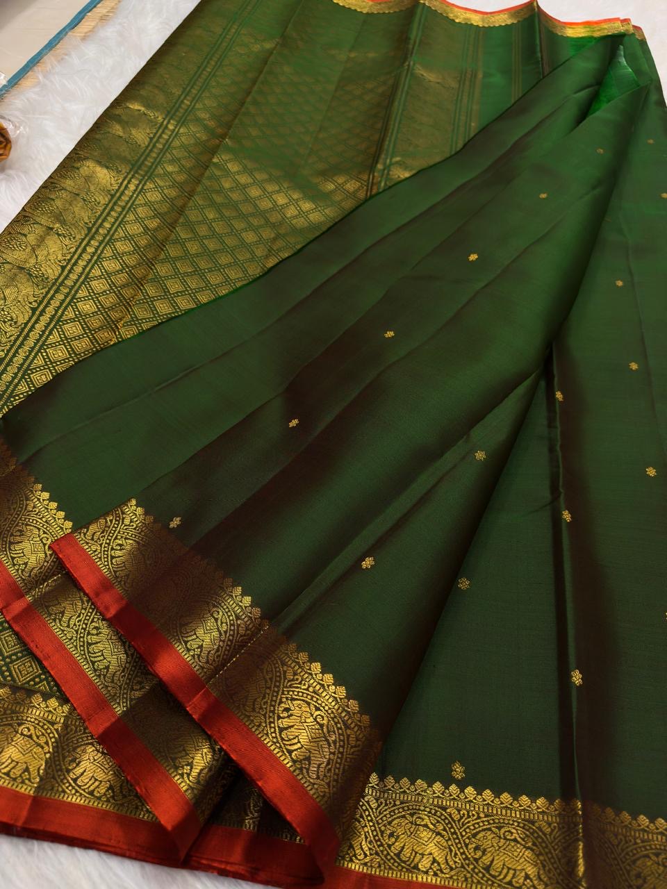 Handwoven Pure Silk Kanchipuram Butta saree with an open dark green body and small gold motifs.