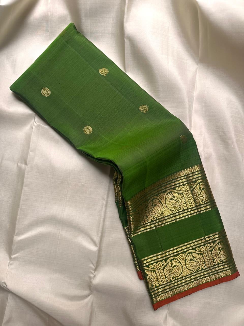 Angled display of fresh leaf green × rust orange handwoven Rettapet Kanchipuram silk with gold zari bands and Mayil Chakram buttas