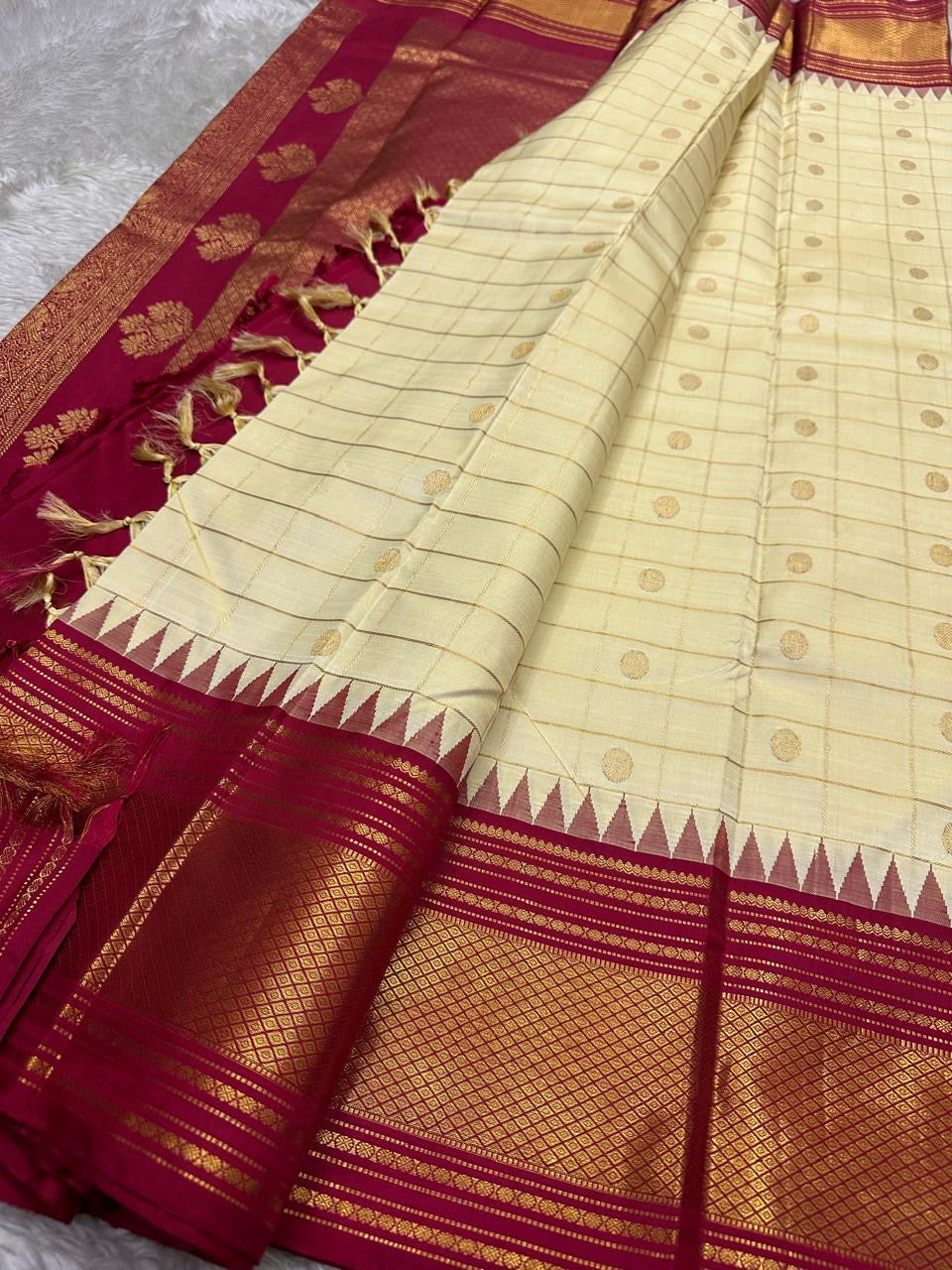 Pure Kanchipuram silk saree laid open with ivory checks, gold zari buttas, temple-edge pattern, and tomato red zari woven border.