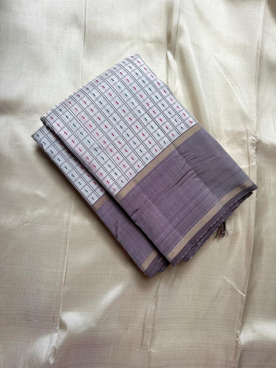 Pure Kanchipuram silk saree folded, featuring an ivory body with fine grid pattern and subtle multicolour dotted accents, paired with a soft grey silk border and classic gold zari lines.