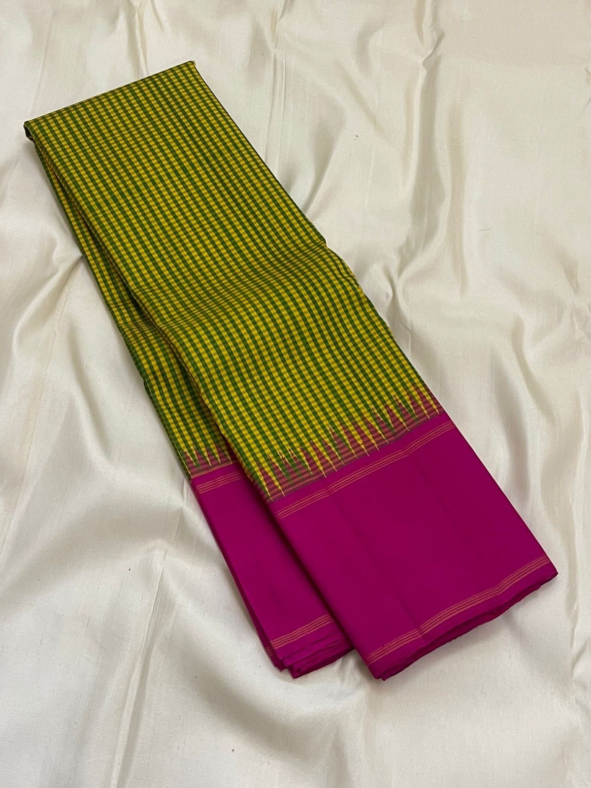 Long folded pure Kanchipuram silk saree showing green-yellow checked body and solid magenta section with thin border lines