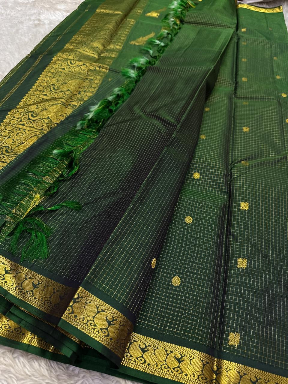 Dark bottle green Kanjipuram silk saree folded showing Zari Kattam grid body with Pavun butta and ornate self-colour Mayil border