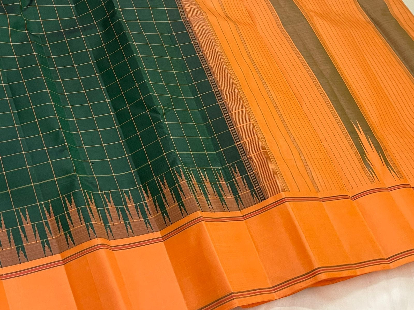 Forest green and orange Kanjipuram silk saree folded showing Kanchi Kattam body and contrast orange border