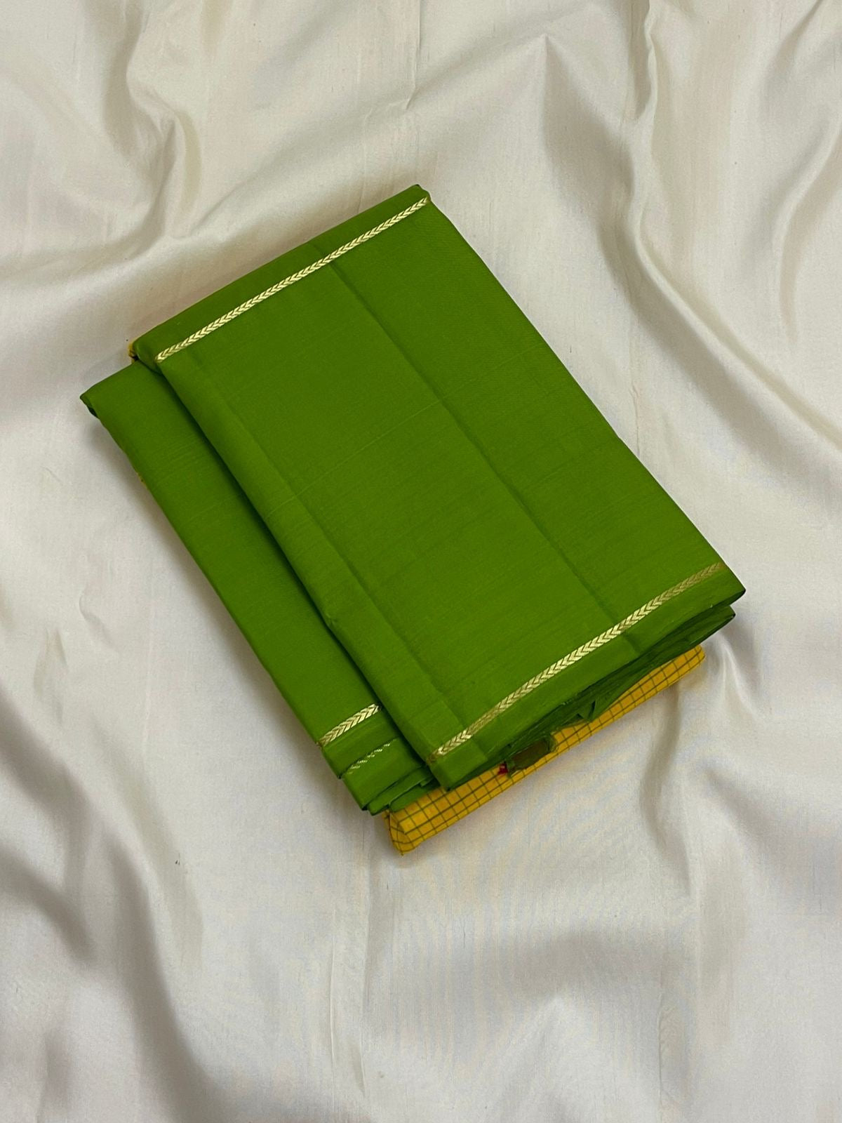Folded green Pure Kanchipuram silk saree with thin zari woven border on white backdrop