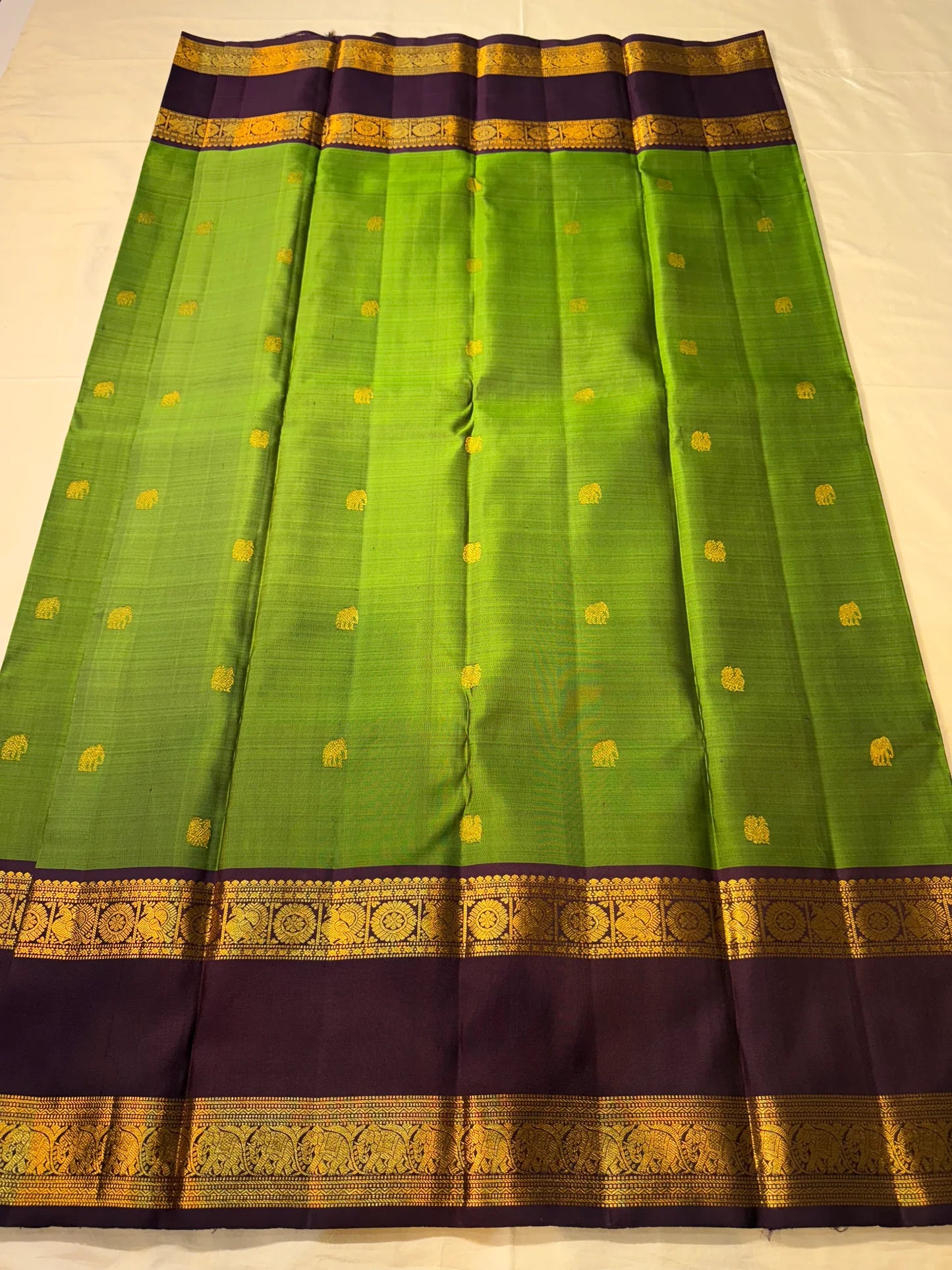 Flat-lay green Pure Kanchipuram silk saree with purple border, gold zari woven bands, and tassel edge, shipped from New Jersey USA