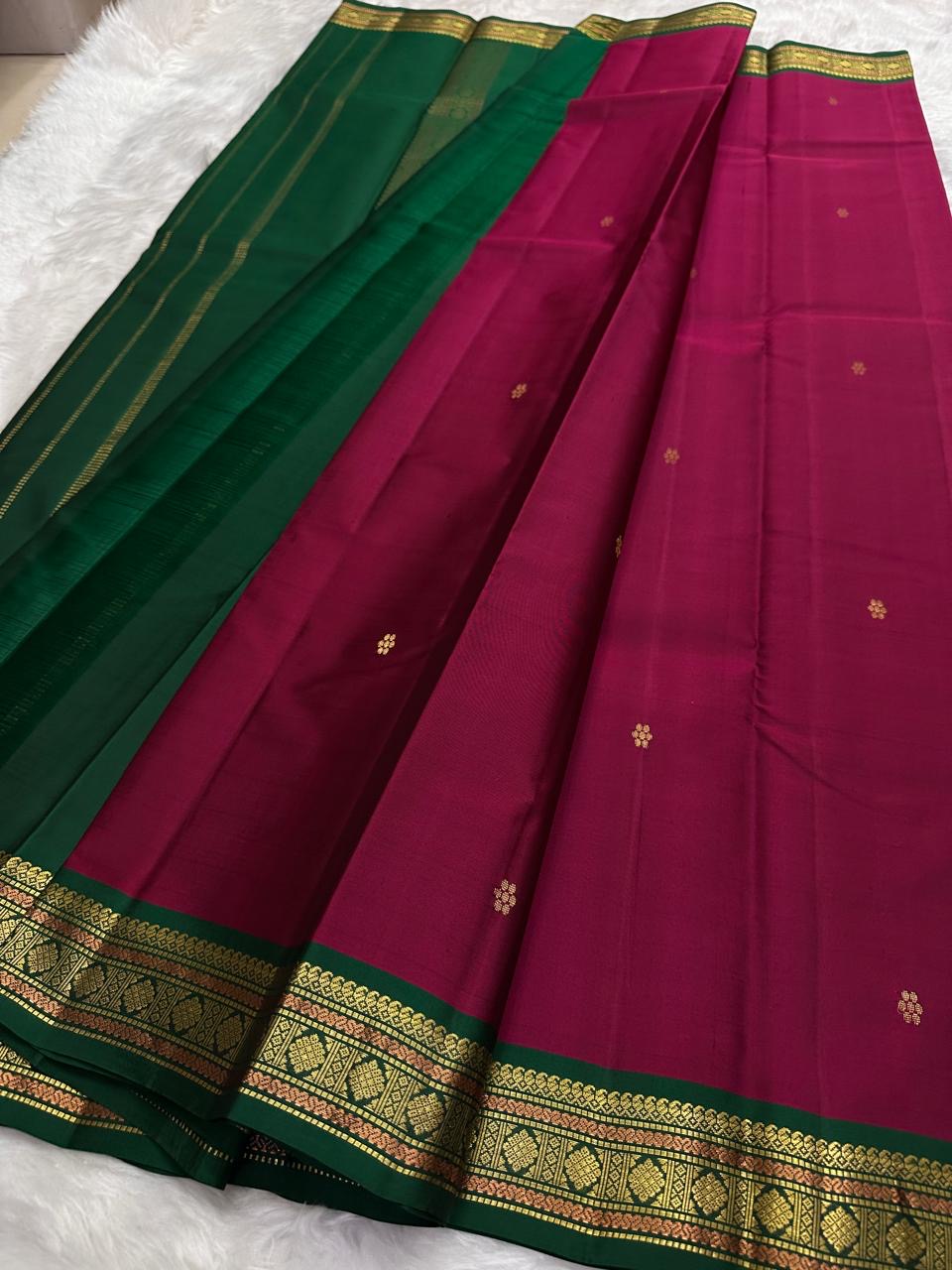 Pure Kanchipuram silk saree draped flat showing deep pink body with evenly spaced gold zari buttas and narrow zari border