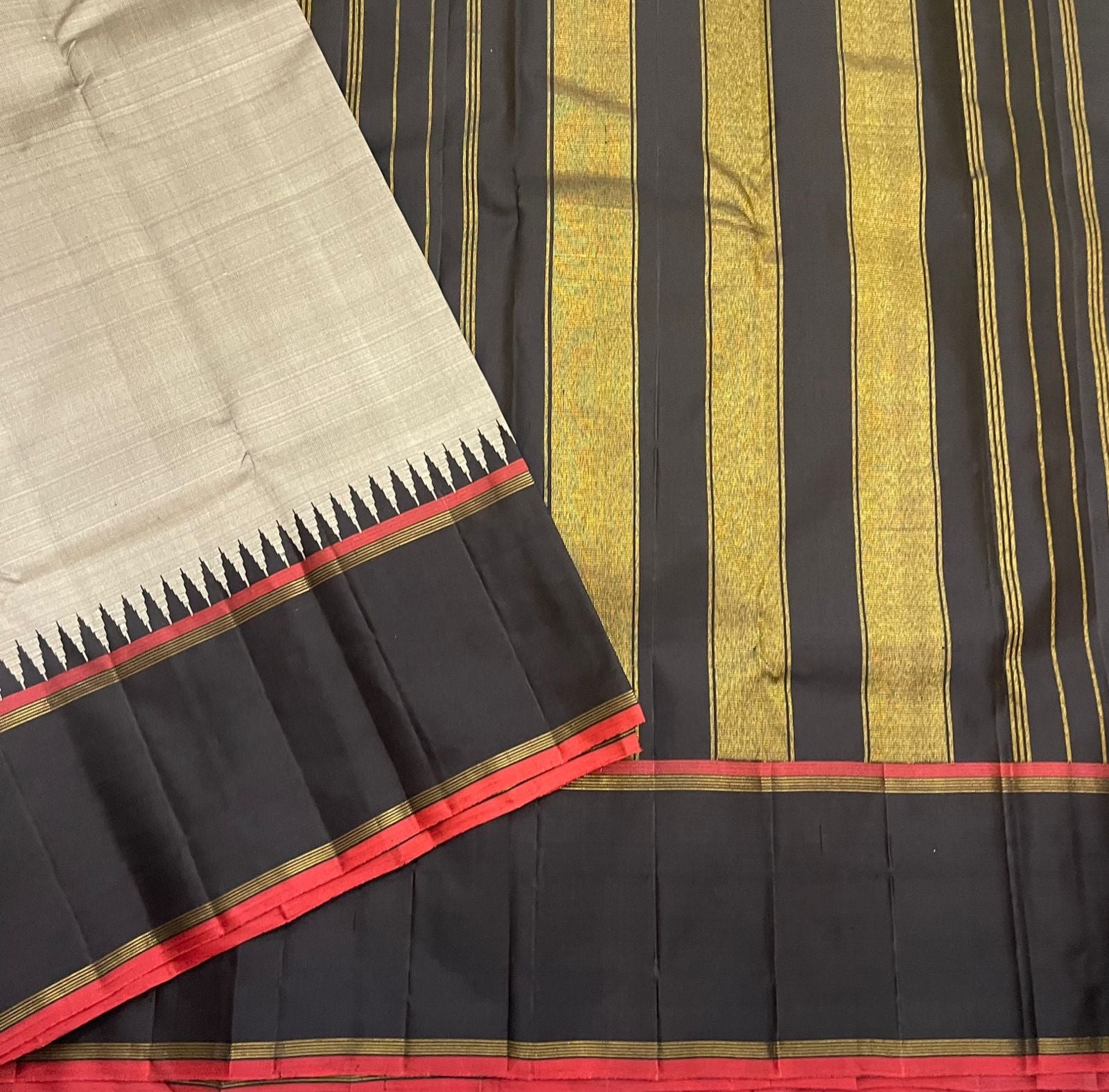 Spread Pure Kanchipuram silk saree with grey body, black border, red selvedge, and gold zari woven stripes on the black panel.
