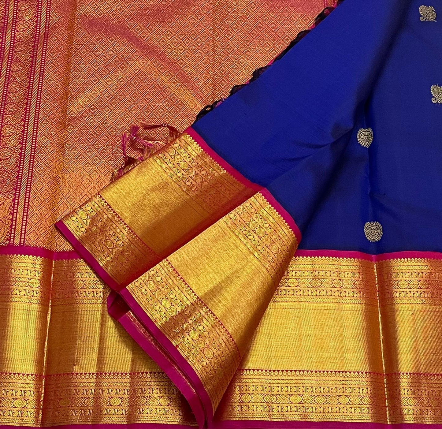 Flat lay of blue Kanchipuram silk saree with gold zari buttas and a gold zari pallu panel framed with pink borders.