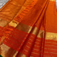 Draped vermilion orange pure Kanchipuram silk saree with gold zari stripe detailing and tassels near the border