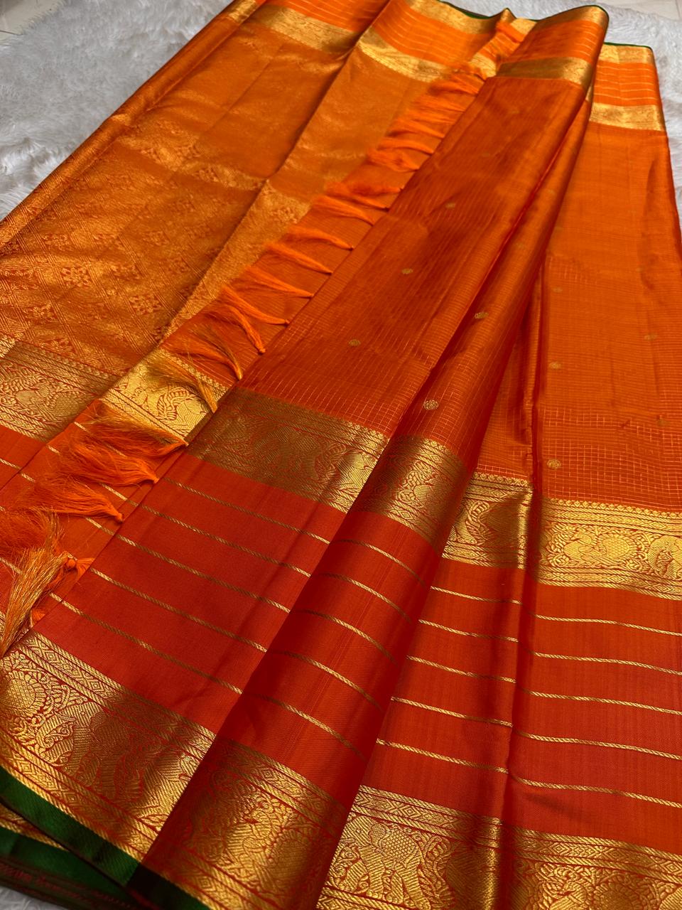 Draped vermilion orange pure Kanchipuram silk saree with gold zari stripe detailing and tassels near the border