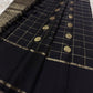 Full flat lay of black Pure Kanchipuram silk saree with zari woven checks, medallion buttas, and black tassels near pallu.