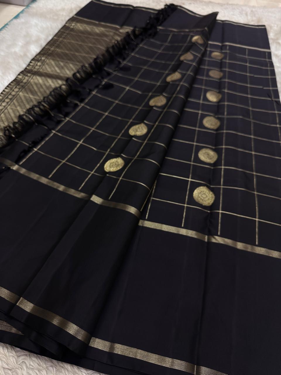 Full flat lay of black Pure Kanchipuram silk saree with zari woven checks, medallion buttas, and black tassels near pallu.