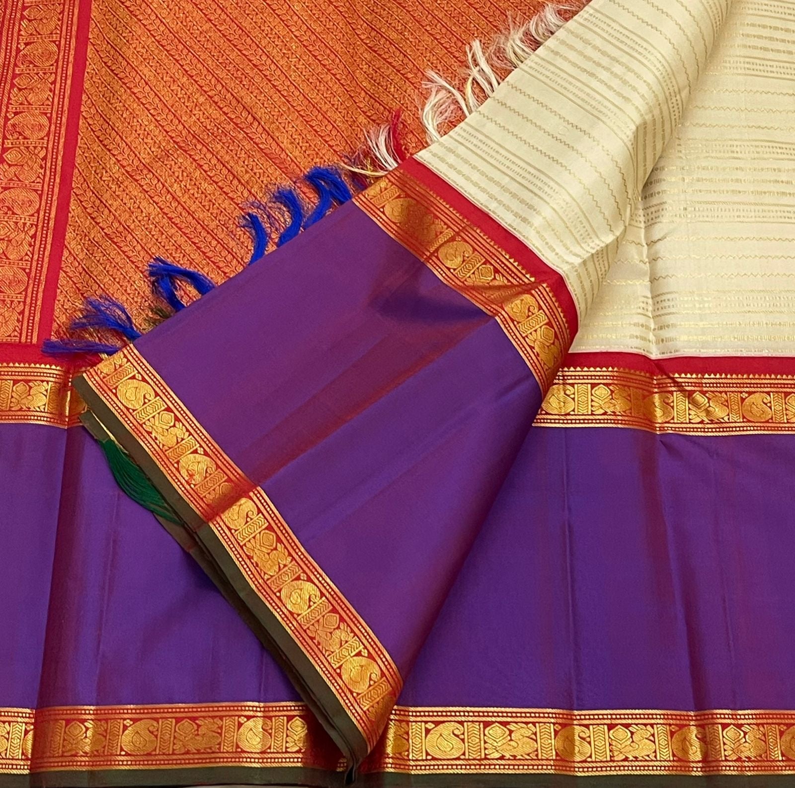 Pure Kanchipuram silk saree showing purple border panels with gold zari woven motifs and blue tassels