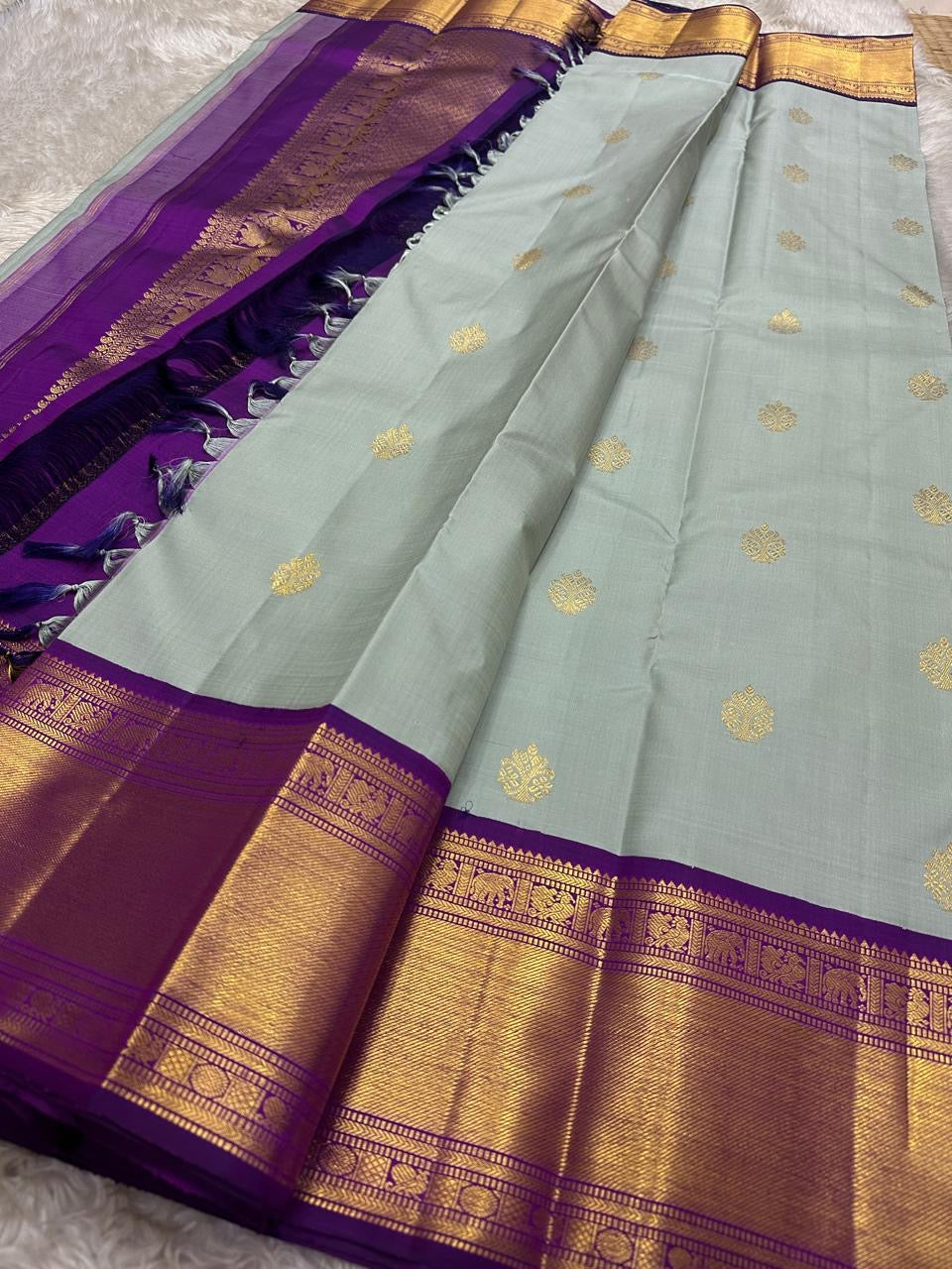 Draped dovetail grey Pure Kanchipuram Silk Saree with scattered gold buttas and purple zari border beside purple pallu