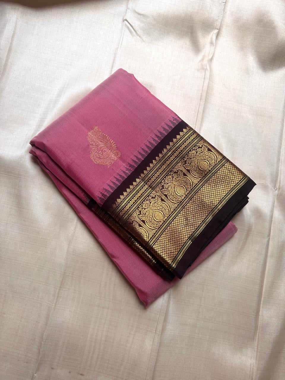 Folded pink Pure Kanchipuram Silk Saree with black zari border and gold paisley motifs, available in the USA