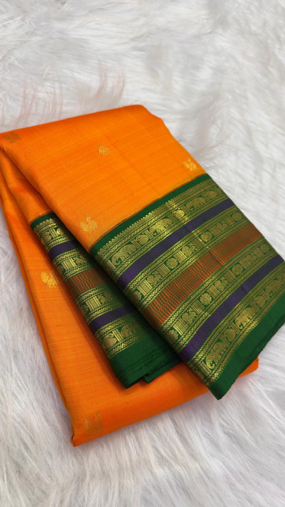 Folded view of marigold orange Kanchipuram saree with green, violet and brick-toned layered zari border.