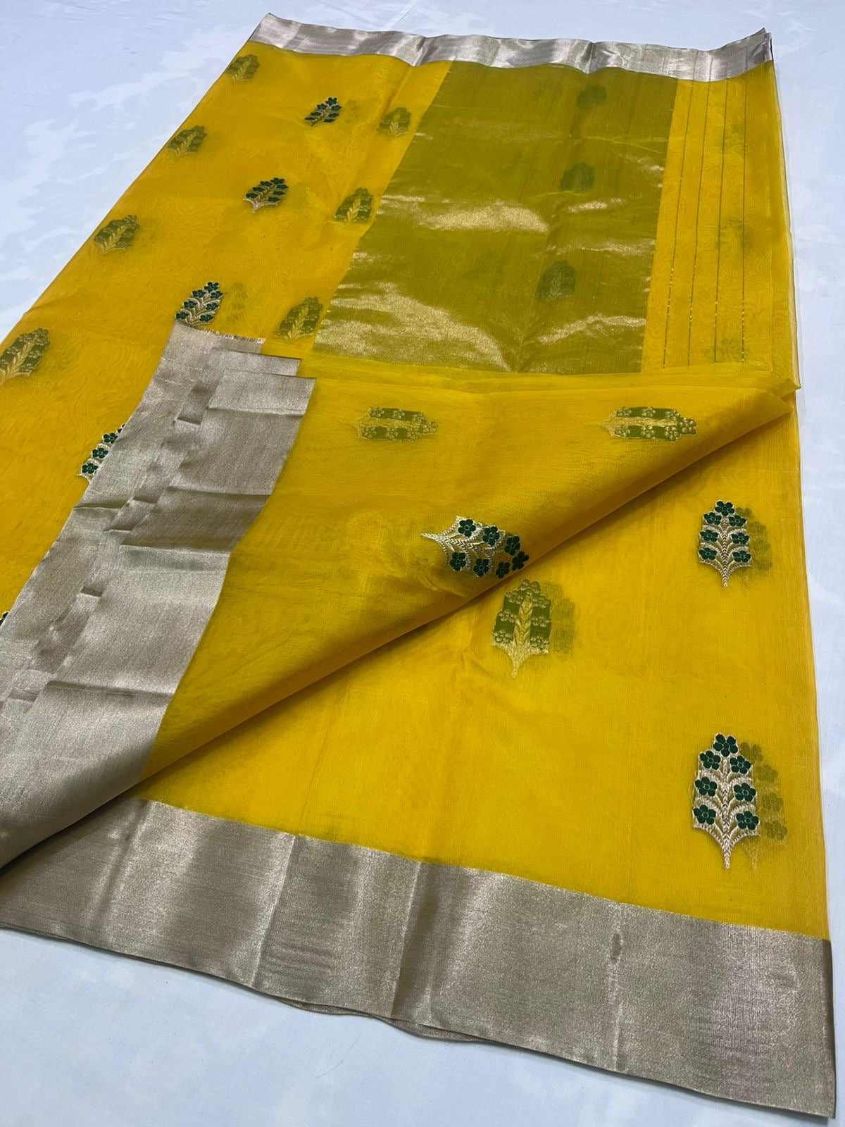 Yellow saree with green leaf patterns and silver border on a white background
