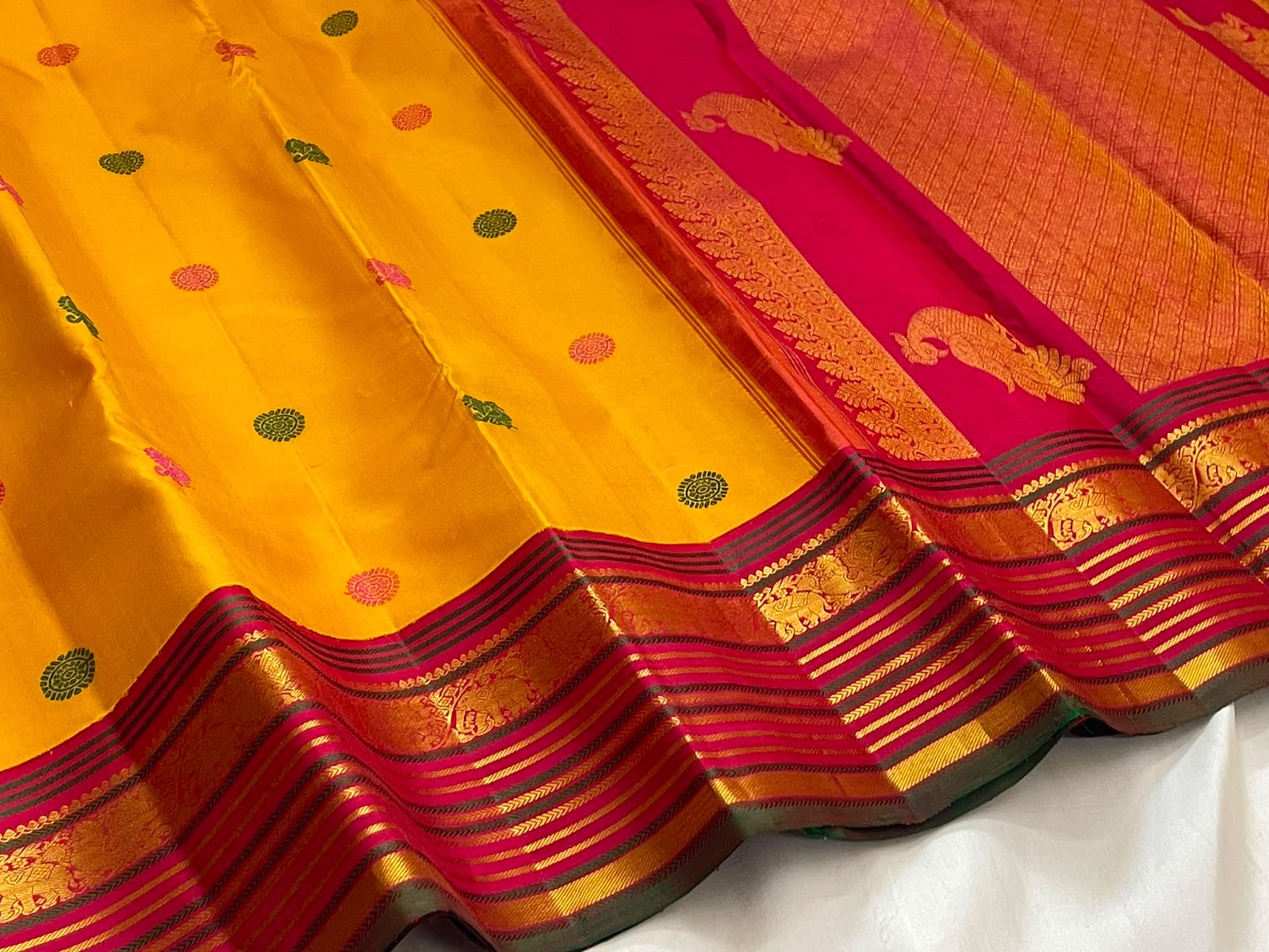 Handwoven golden turmeric Kanchipuram saree with raspberry pink zari border.