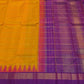 Folded saffron-orange Kanchipuram Korvai saree with a purple border and pink Thazhampoo Reku edging.