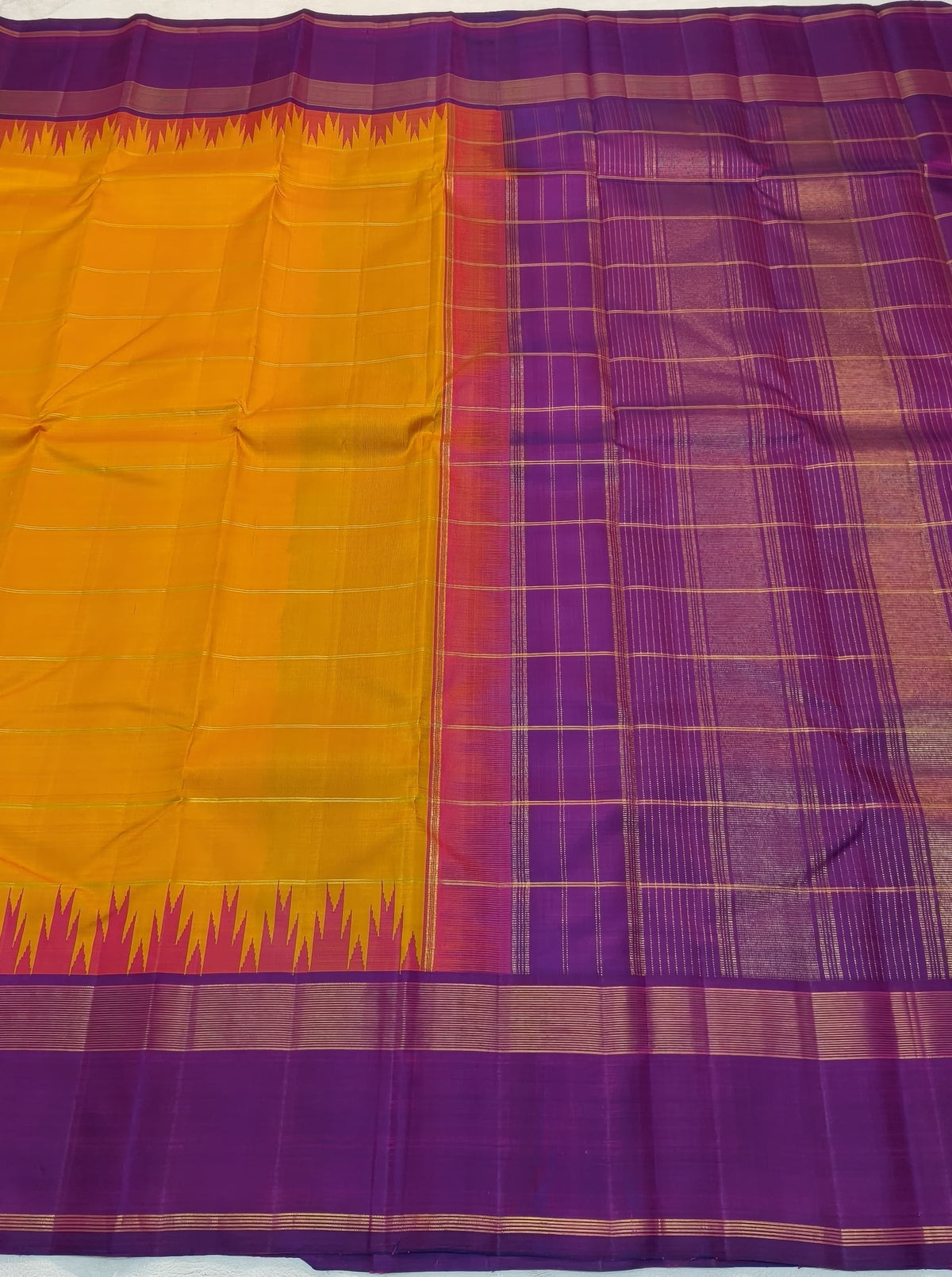 Folded saffron-orange Kanchipuram Korvai saree with a purple border and pink Thazhampoo Reku edging.