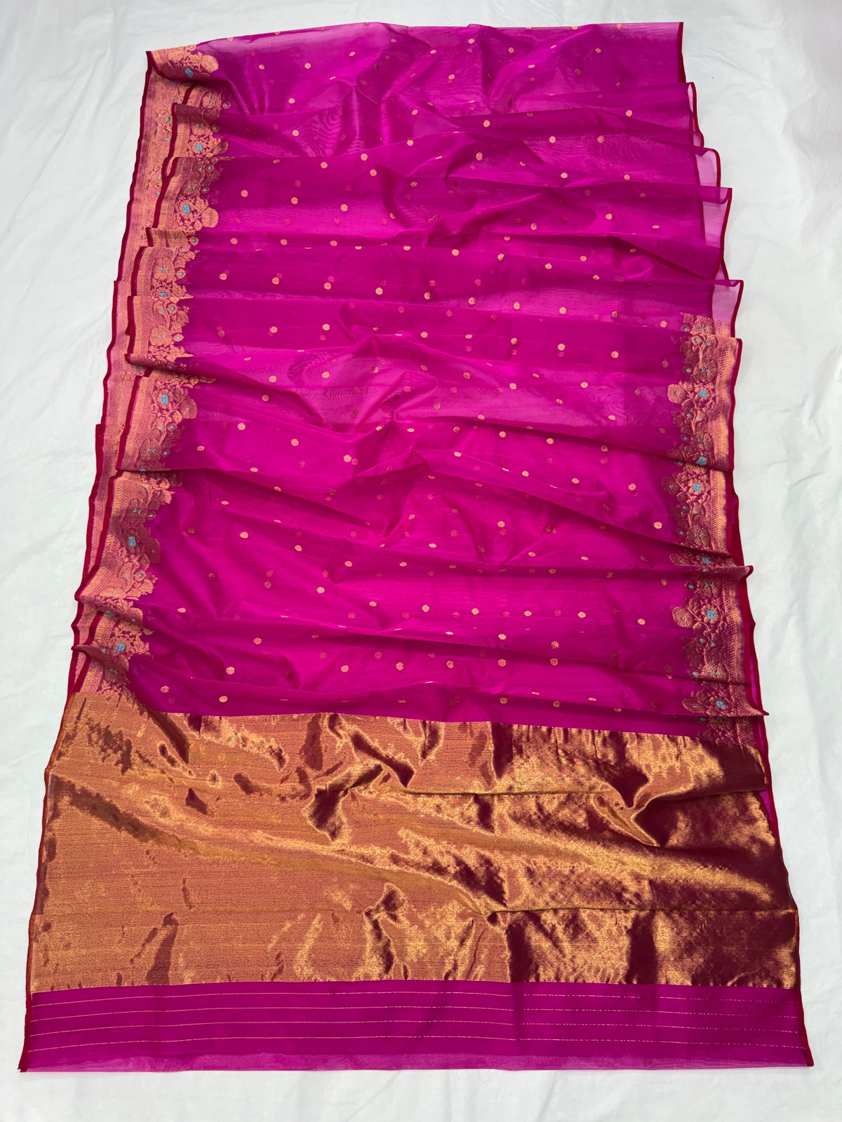 Purplish pink Katan silk Chanderi saree laid open showing small gold-toned buttas and broad antique-gold floral border with turquoise accents