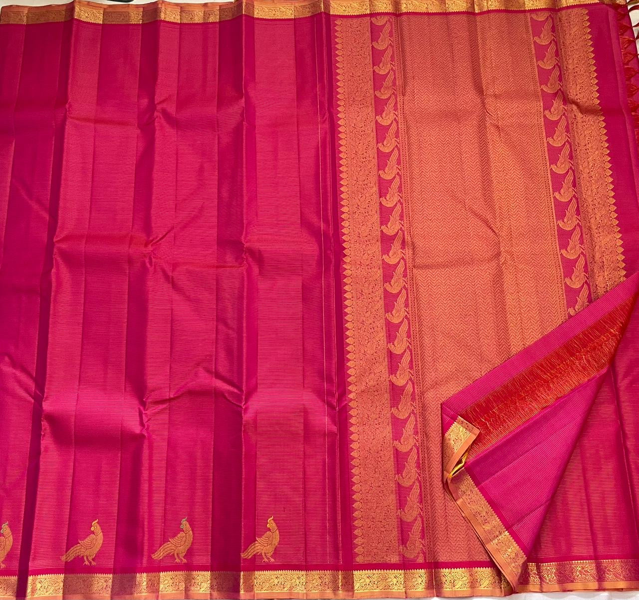 Folded hot pink KanchiPattu pure silk saree showing Vairaoosi zari shimmer body and copper contrast border