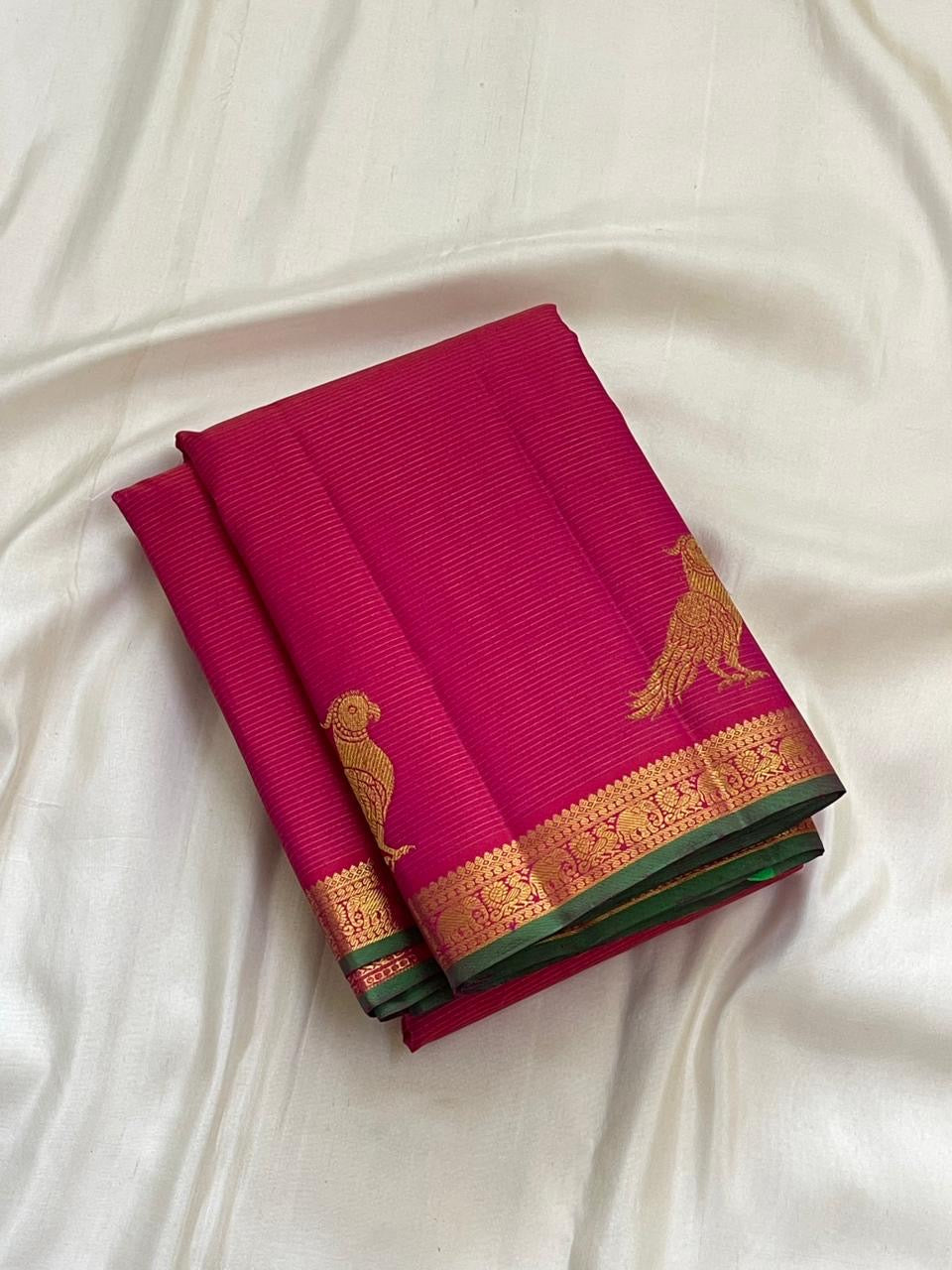 Folded hot pink Kanchipuram pure silk saree showing Vairaoosi zari shimmer body and green contrast border