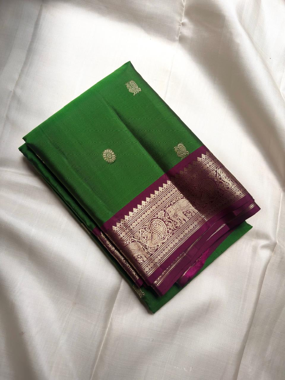 Handwoven green Kanchipuram silk saree with antique-gold zari buttas and purple border.