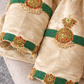 Cream silk velvet sleeve close-up with green bead bands, kundan medallions, red stones, and pearl tassels