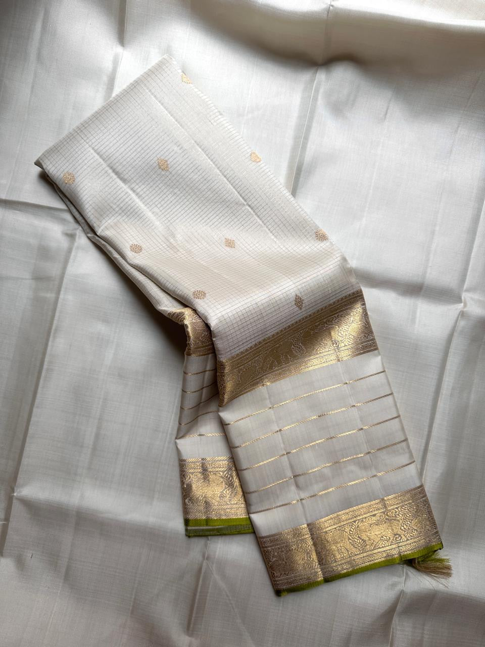 Soft ivory Kanchipuram silk saree with zari kattam grid, small antique gold buttas, and wide gold zari border with lime green selvedge
