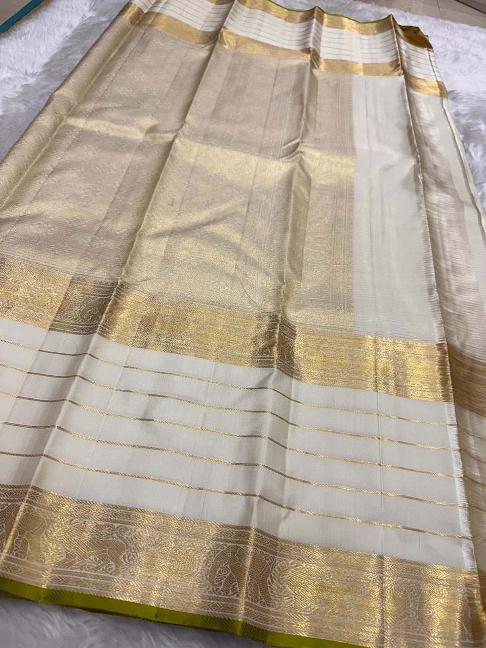 Close view of ivory Kanchipuram silk saree pallu with gold zari weaving, subtle grid texture, and lime green edge