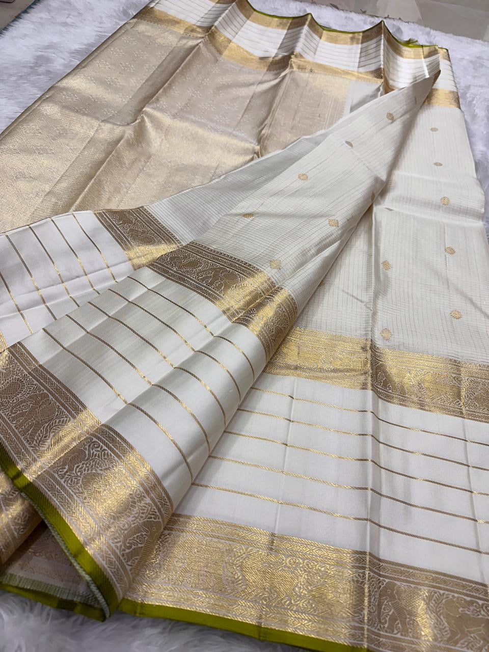 Opened pearl ivory Kanchipuram saree displaying gold zari borders, a grid-woven body and fresh leaf-green edge.