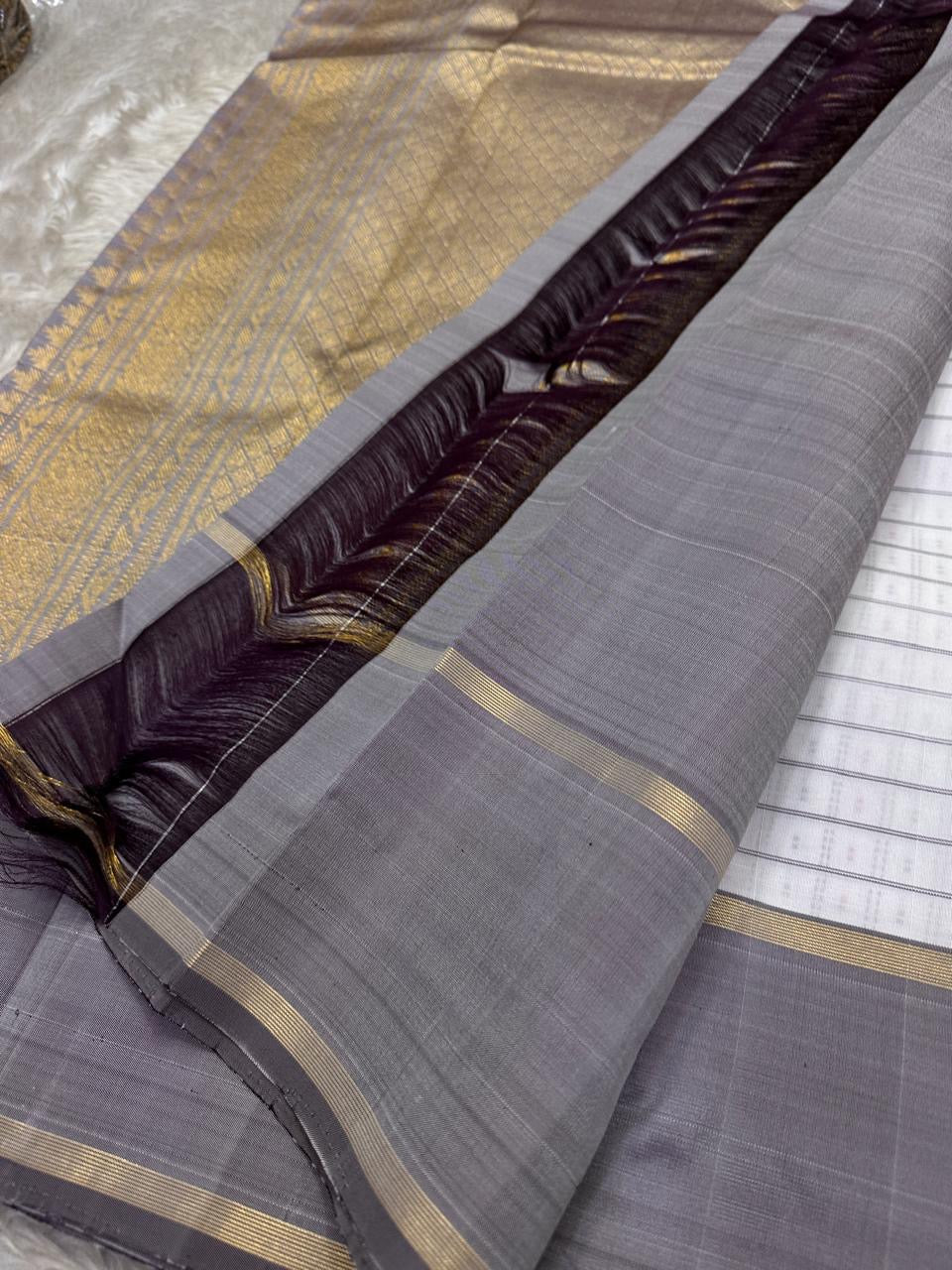 An ivory Kanchipuram silk saree featuring a fine grid pattern with subtle multicolour dotted accents, complemented by a soft grey border and gold zari detailing. The contrast pallu adds depth while maintaining visual balance.