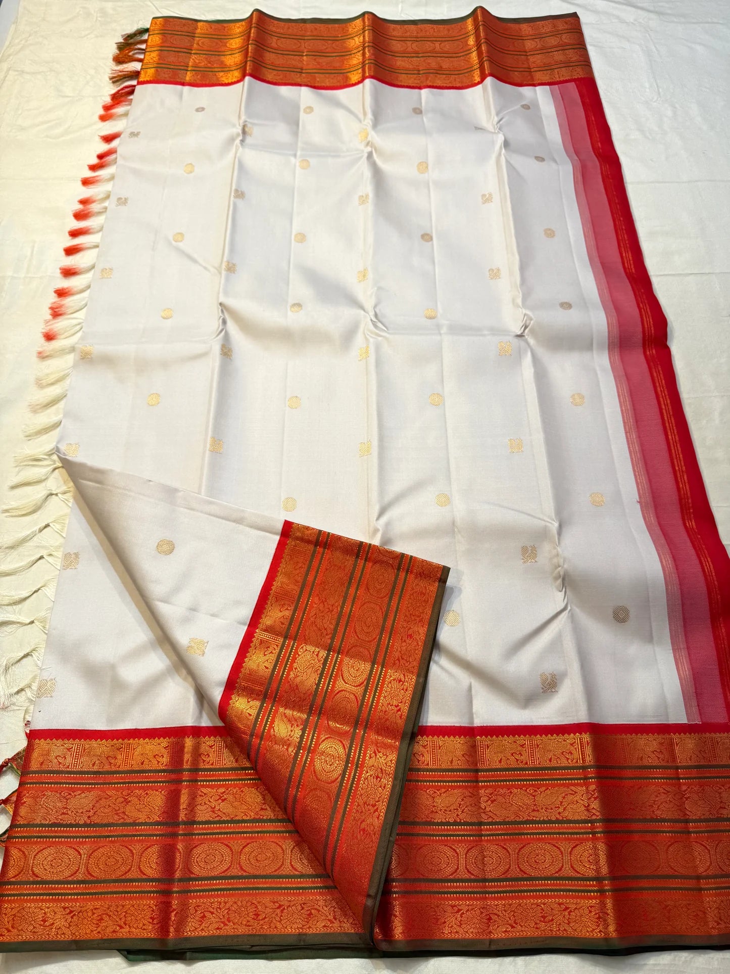 Pure Kanchipuram Silk Saree laid flat with ivory body, gold buttas, zari border, red side border, and tassels
