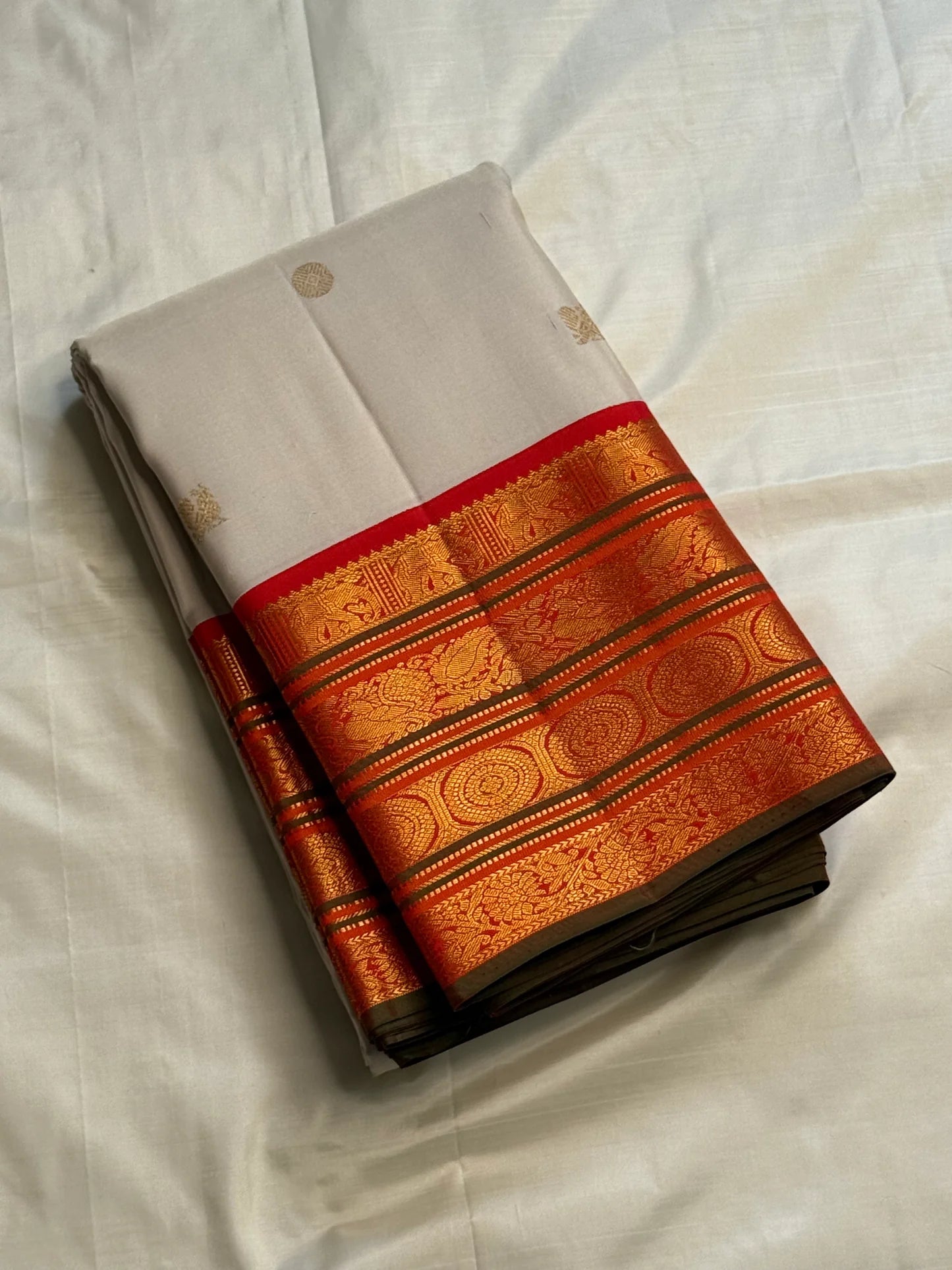 Folded ivory Pure Kanchipuram Silk Saree with small gold buttas and zari border with red edge