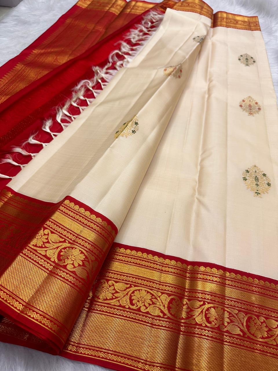 Ivory pure silk body showing spaced floral zari buttas and subtle green Meenakari accents.