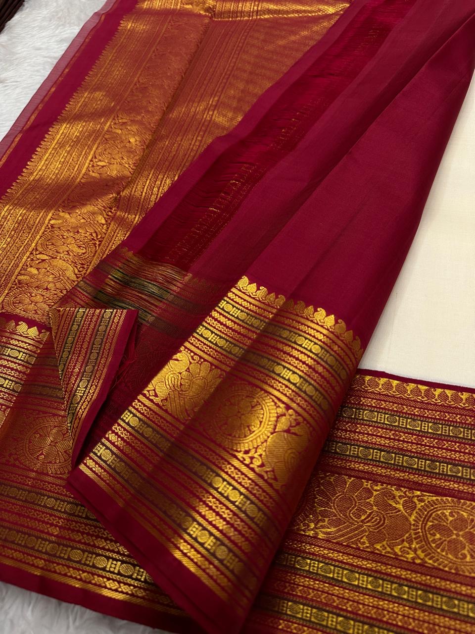 Handwoven ivory Kanchipuram body with small gold-zari buttas above a broad Arakku-red ornamental border.